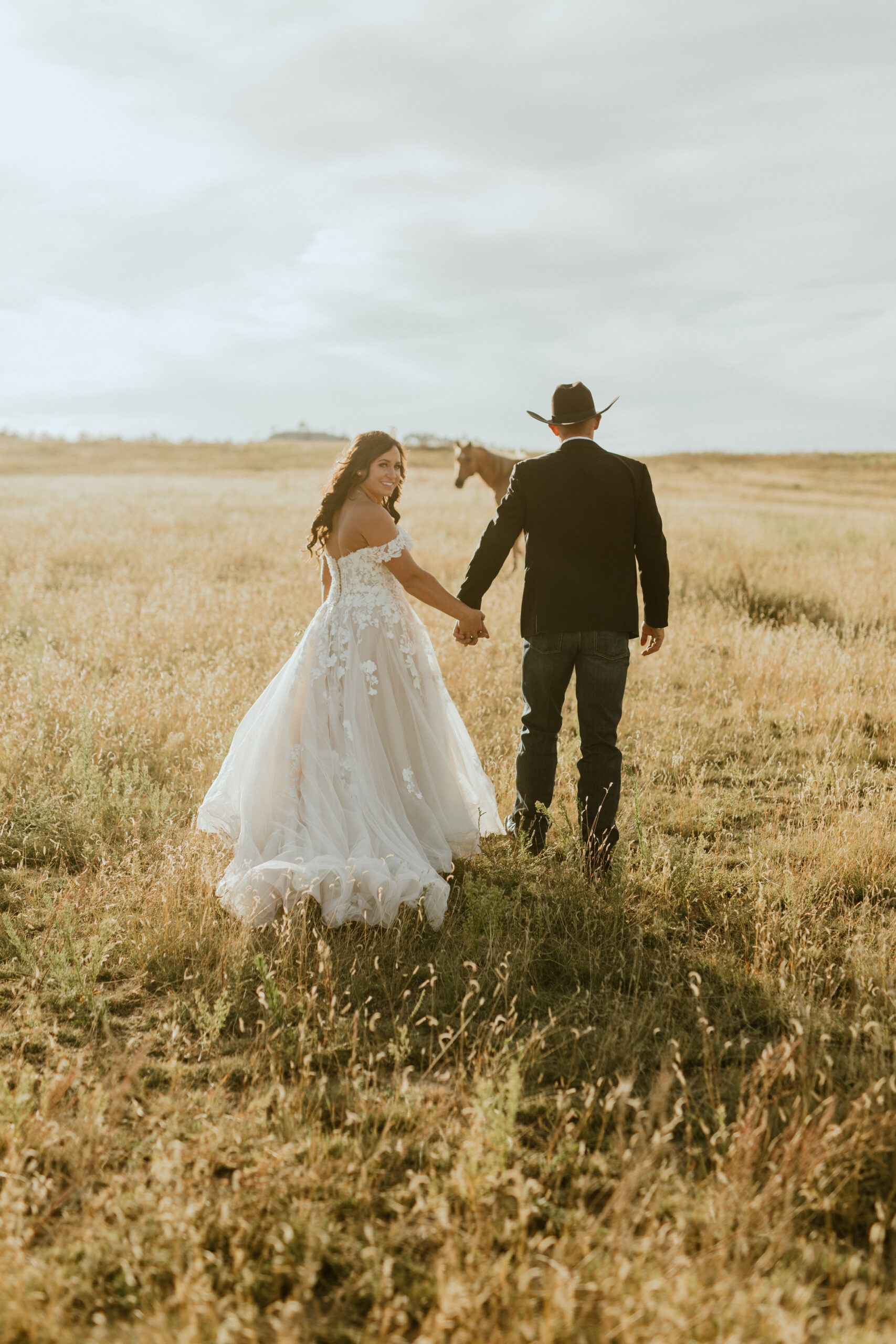 bride and groom wedding photo in midwest field with horse in distance at the golden hour
