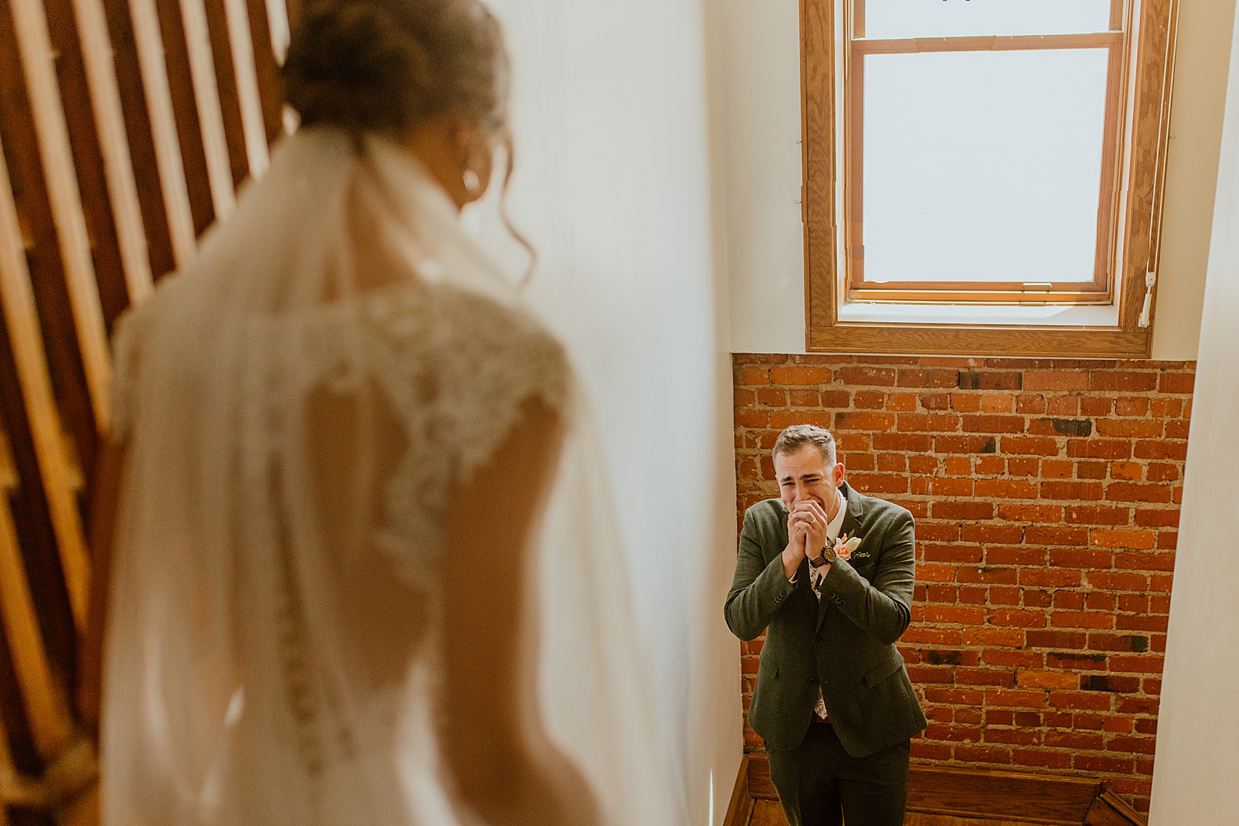 first look photo on wedding day with bride at top of the stairs and emotional groom at bottom