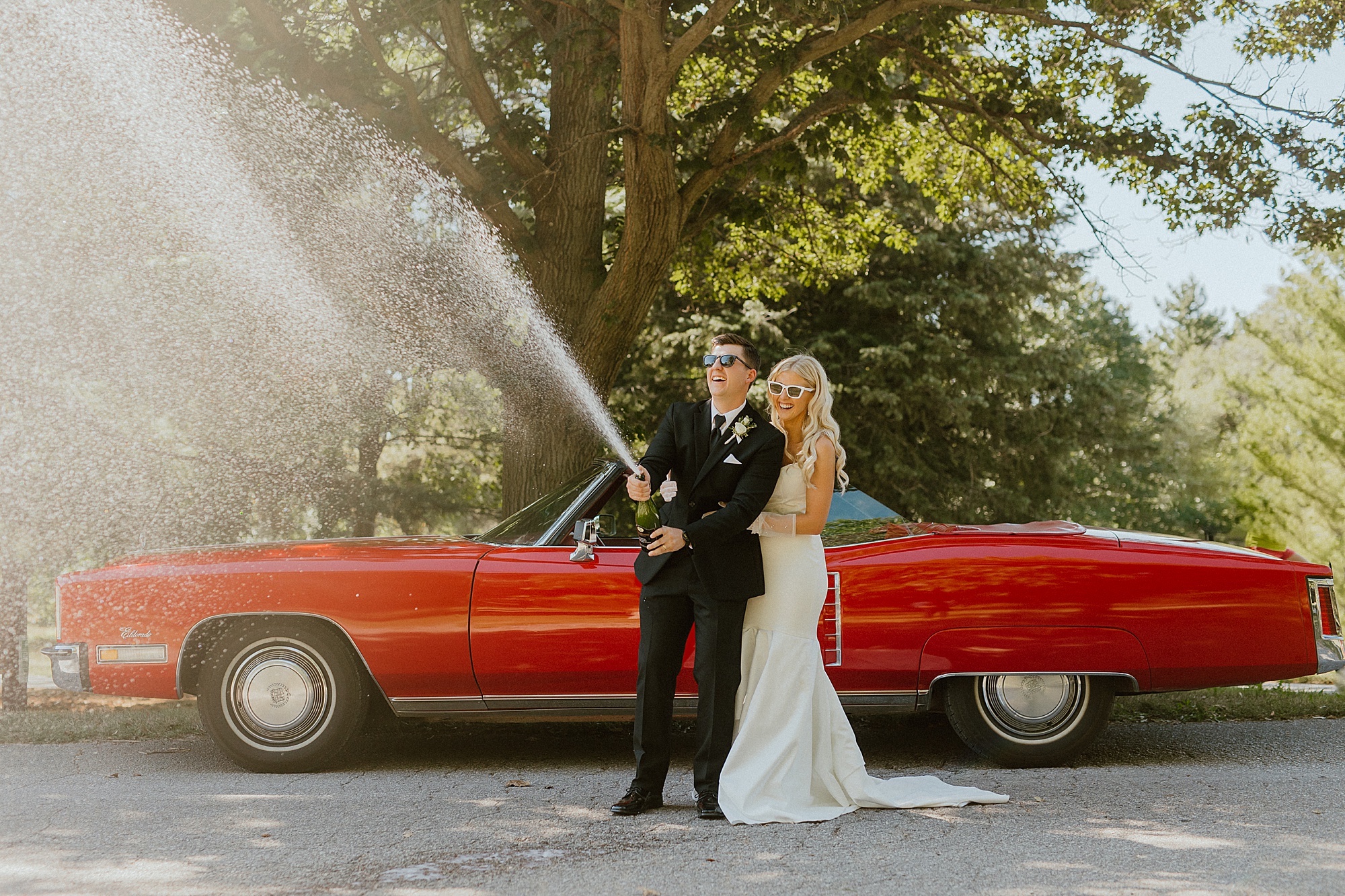 bride and groom enjoy the perfect wedding gift by red classic car champagne