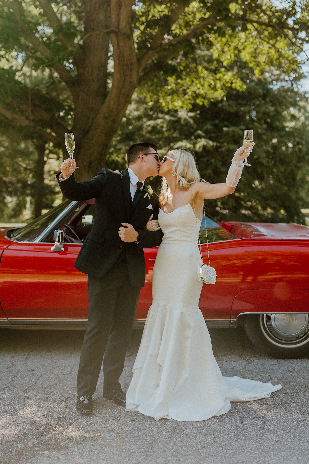 bride and groom celebrate perfect wedding gift of champagne glasses near red classic car