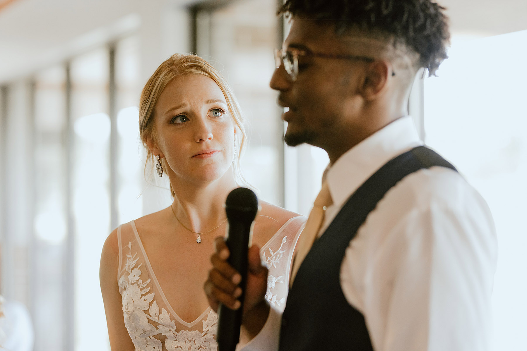 bride stares loving at groom as he speaks with microphone, mixed race couple, wedding day