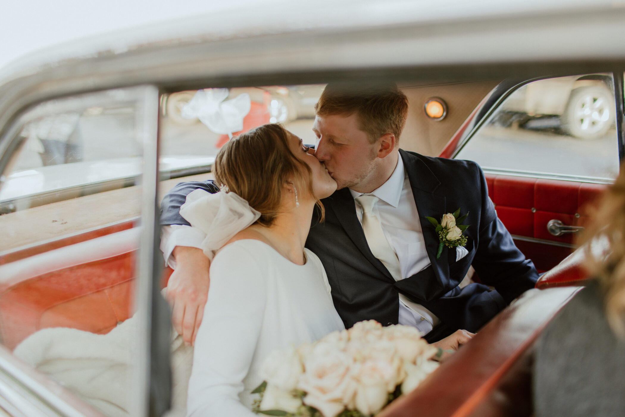 bride and groom kissing in car after wedding photographer associate captures the moment on their special day