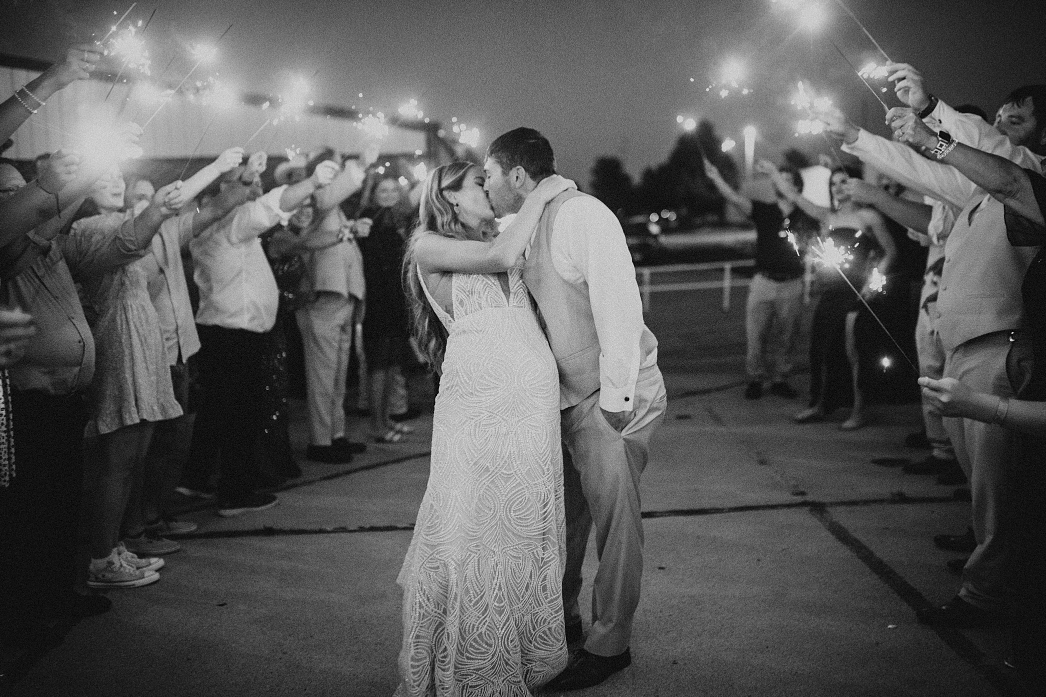 wedding photographer demonstrates lighting technique learned during professional development of lighting, focus, black and white bride and groom with sparklers around them